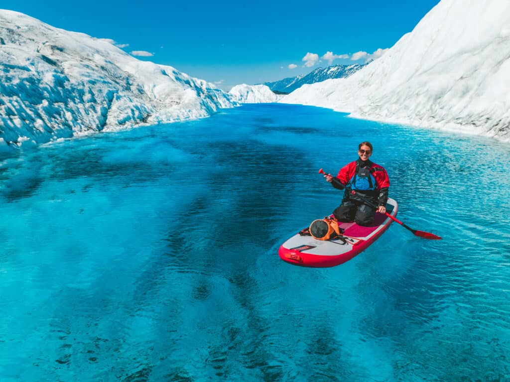 a woman paddle boarding in a blue glacier pool